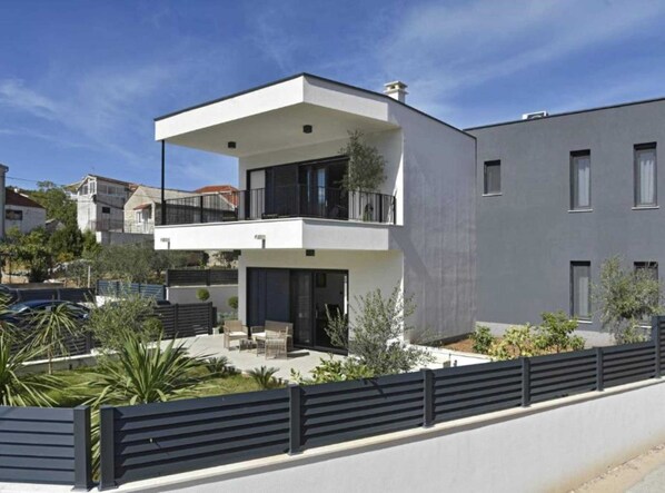 A modern two-story building with a balcony, a covered outdoor seating area, and a fenced garden. - Luxury Slatine Apartments With Terrace and Garden (Split)