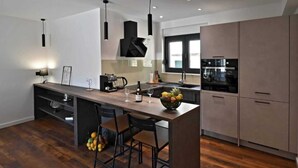 A modern kitchen with a central island, bar stools, a coffee machine, and a fruit bowl. - Luxury Slatine Apartments With Terrace and Garden (Split)