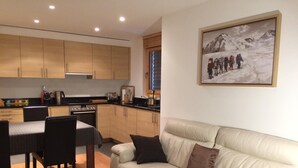 A modern kitchen with wooden cabinets, a dining area with a table and chairs, and a living room with a sofa and cushions. - Lovely Apartment With Mountain Views (Veysonnaz)