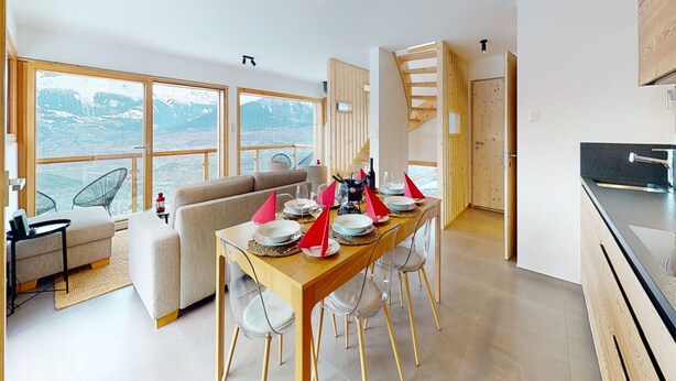 Et moderne køkken med spiseplads, store vinduer med udsigt til et bjerglandskab, og en trappe til en etage ovenover.
