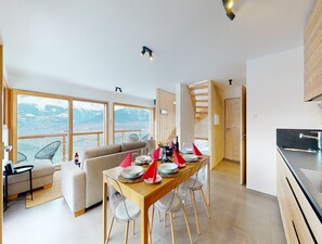 A modern kitchen with a dining area, large windows with a mountain view, and a staircase leading to an upper level.