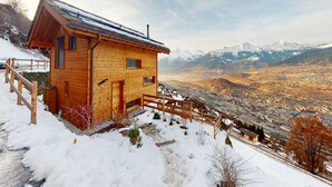 En træhytte med en træterrasse og udsigt over en dal og bjerge.