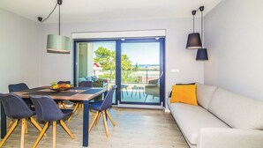 A modern living room with a dining area, large sliding glass doors leading to an outdoor space, and a sofa with a yellow pillow. - Modern Kastel Villa With Private Pool, Gym, and Large Outdoor Space (Kastela)