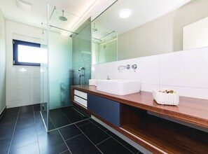 Ein modernes Badezimmer mit Duschkabine aus Glas, einem weißen Waschbecken und einem Holzwaschtisch.