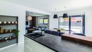 A modern kitchen with a central island, built-in shelves, and pendant lighting. - Modern Kastel Villa With Private Pool, Gym, and Large Outdoor Space (Kastela)