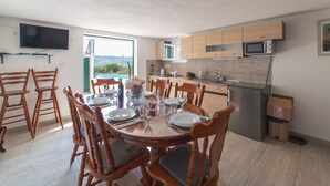 A dining area with a round table set for six, wooden chairs, a TV mounted on the wall, and a kitchen with wooden cabinets and a microwave. - Serene Retreat Holiday Home With Pool (Klis)
