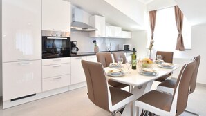 Une cuisine moderne avec des meubles blancs, une table à manger dressée pour six personnes et un lustre.