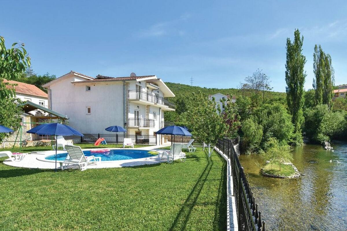 Un bâtiment à deux étages doté d’une piscine, entouré d’une pelouse verdoyante et bordé par une rivière.