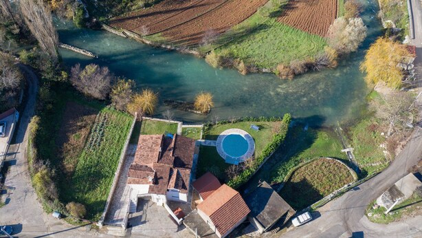 Vue aérienne d’une propriété riveraine dotée de terrasses cultivées, d’une piscine et d’un petit bâtiment surmonté d’un toit en tuiles.