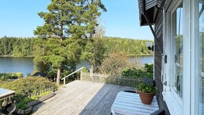 A wooden deck with a table and chairs, overlooking a lake and forest. - 4 Star Holiday Home in Ljusfallshammar (Ljusfallshammar)