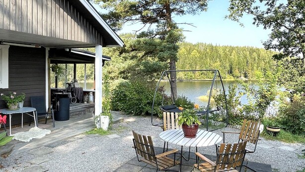 A patio with a table and chairs, a swing, and a view of a lake. - 4 Star Holiday Home in Ljusfallshammar (Ljusfallshammar)