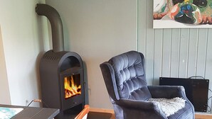 Um quarto aconchegante com lareira a lenha, uma poltrona confortável e uma mesa de jantar.