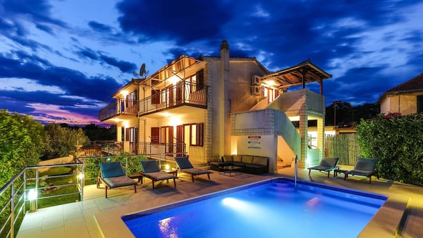 Une maison à deux étages avec une piscine, un espace extérieur aménagé et une zone couverte.