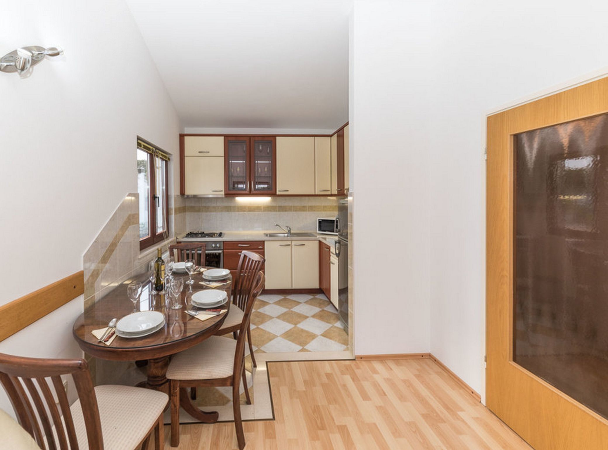 Una cocina compacta con armarios de madera, una mesa de comedor para cuatro personas y un suelo a cuadros.