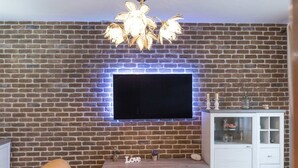Un salon avec un mur en briques, un téléviseur à écran plat fixé au-dessus d’un meuble de rangement en bois, un meuble blanc et un canapé marron.