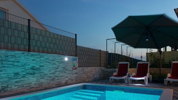 Ein Swimmingpool mit Fliesenstufen, umgeben von Liegestühlen und einem Sonnenschirm.