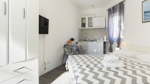 Ein gemütliches Hotelzimmer mit Bett, Schreibtisch, Stuhl, Küchenzeile und Fernseher.