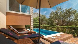 Un espace aménagé au bord de la piscine, avec des chaises longues et une table, une piscine, et une vue sur des arbres et un bâtiment.