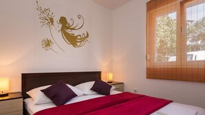 Un letto rifatto con cura, una coperta rossa, due cuscini bianchi e un adesivo decorativo al muro.
