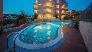 Una piscina con bordo piastrellato, circondata da un edificio a più piani con balconi e zone relax all'aperto.