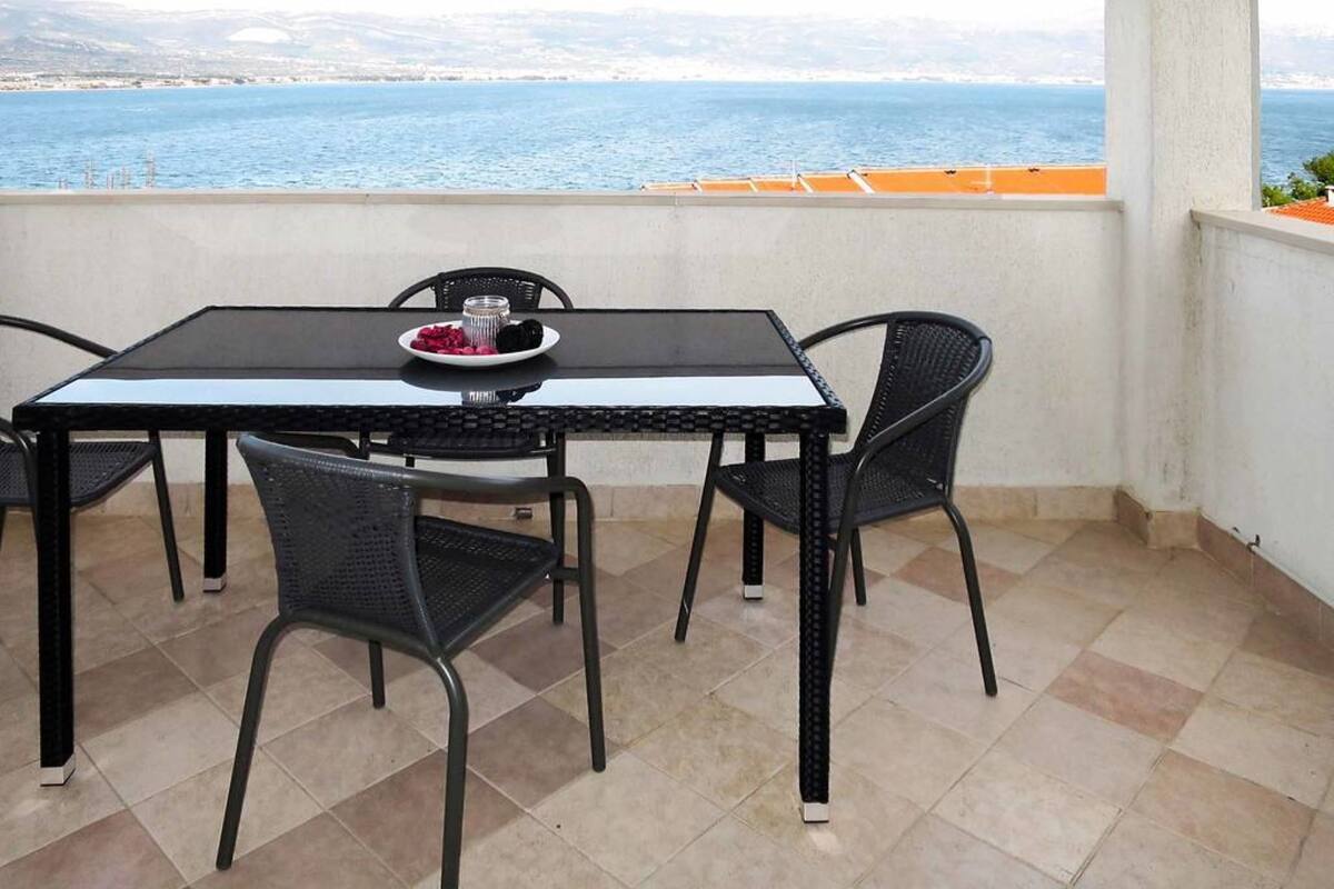 A balcony with a table and chairs, overlooking a body of water and distant hills.