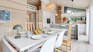 A modern kitchen with white cabinets, a central island, and a dining area with a white table and chairs. - "Aruna" - 550m from the sea by Interhome (Idestrup)