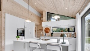 A modern kitchen with a central island, white cabinetry, and a large window offering a view of the outdoors. - "Aruna" - 550m from the sea by Interhome (Idestrup)