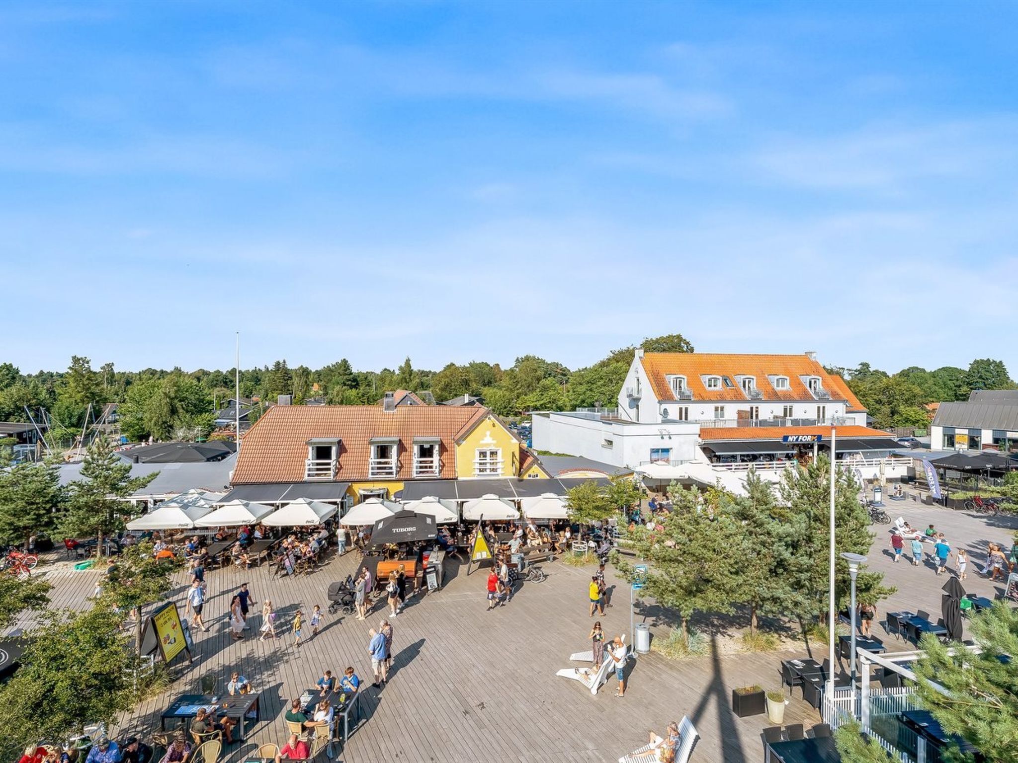 Een levendige marktplaats buiten met houten terrassen, diverse kraampjes en een menigte mensen.
