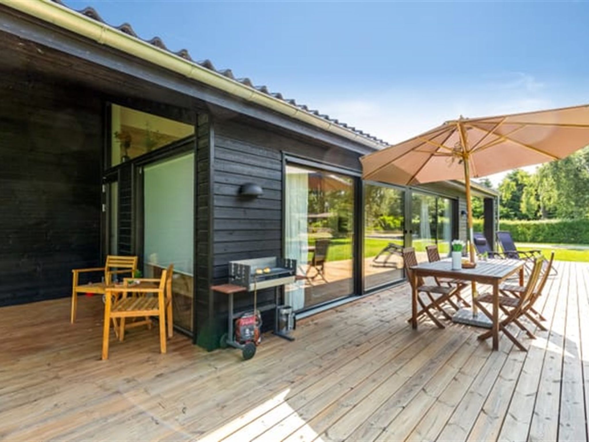 Een houten terras met buitenmeubilair, een barbecue en een grote parasol.