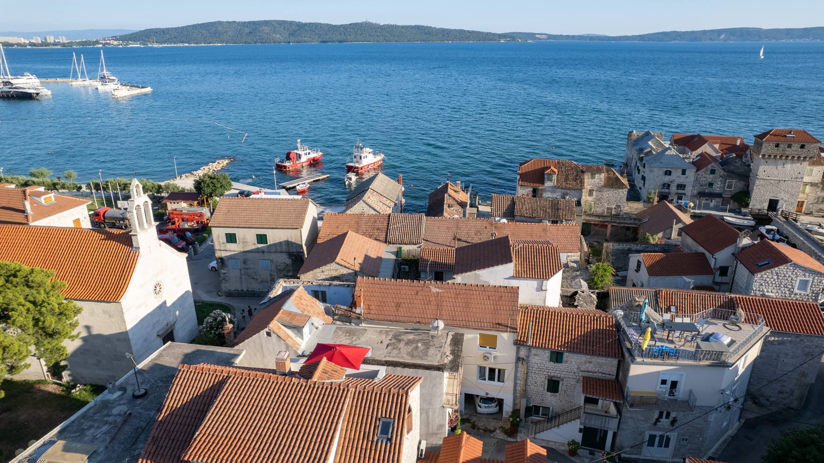 Uma cidade costeira com arquitetura tradicional, um porto com barcos e uma vista clara do mar.