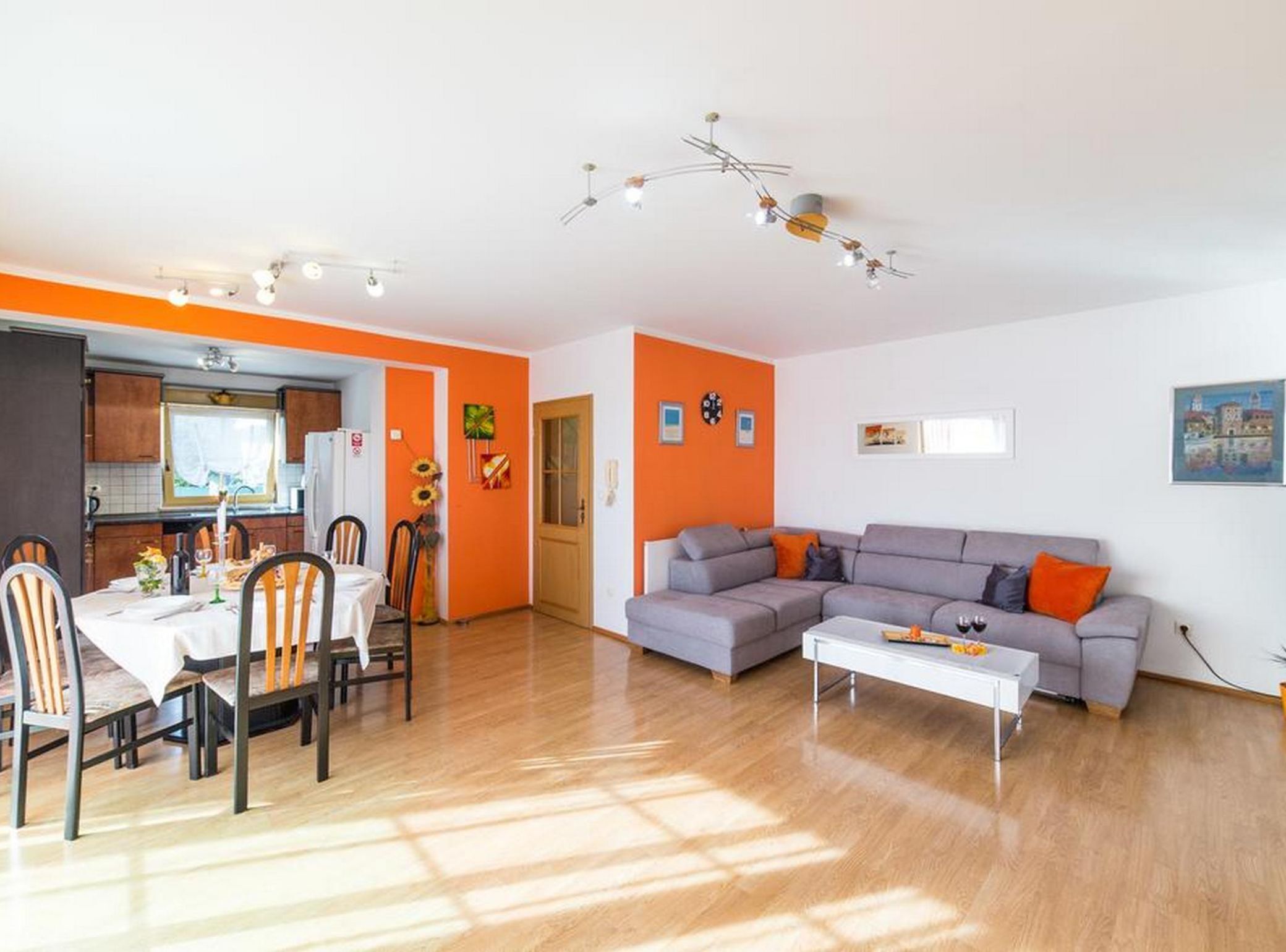 Un salon moderne avec un canapé gris, une table à manger avec des chaises et un coin cuisine visible à travers une porte ouverte.