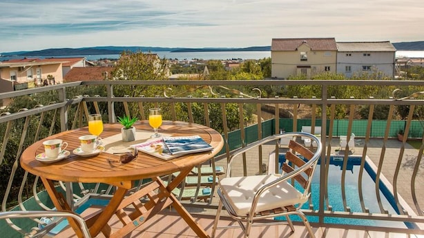 Ein Balkon mit Holztisch, zwei Stühlen, einer Zeitschrift und einem Glas Orangensaft.