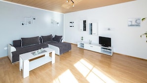 Ein modernes Wohnzimmer mit Holzbalkendecke, einem grauen Sofa, einem weißen Couchtisch, einem Fernseher und einer weißen Kommode.
