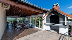 Eine Terrasse im Freien mit überdachter Sitzgelegenheit, Grill und Esstisch mit Stühlen.