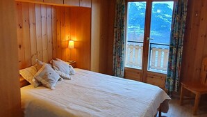 A wooden room with a bed, a nightstand with a lamp, and a view of a balcony with curtains. - Mont Bijou Mountain & Quiet Chalet 10 Pers (Veysonnaz)