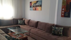 A modern living room with a sectional sofa, a glass coffee table, and decorative pillows. - Magnificent apartment with green spaces 2 minutes walk from Houara-Tanger beach (Tanger)