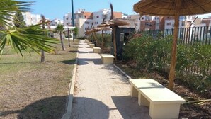A pathway lined with benches and thatched umbrellas, leading to a building with a white facade. - Magnificent apartment with green spaces 2 minutes walk from Houara-Tanger beach (Tanger)