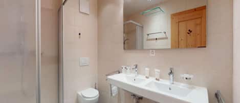 A modern bathroom with a glass shower enclosure, a white toilet, and a large vanity with dual sinks.