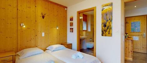 Una habitación con dos camas, paredes y puerta de madera, y un baño visible a través de una puerta abierta.