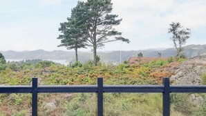 Eine Holzterrasse mit Geländer, mit Blick auf eine gebirgige Landschaft mit Vegetation und einem weit entfernten Gebäude.