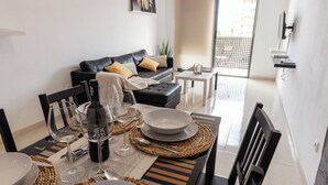 A dining area with a table set for four, a black leather sofa, and a view of the outside through a window. - Apartamentos LA PARRETA CENTRO (Vinaros)