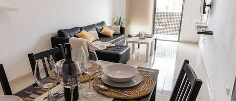 A dining area with a table set for four, a black leather sofa, and a view of the outside through a window.
