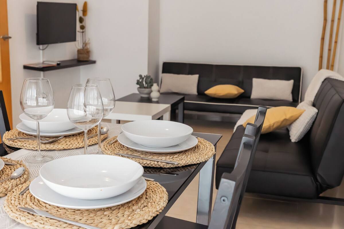 Un coin repas avec une table dressée pour quatre personnes, comprenant des assiettes, des verres et des couverts.