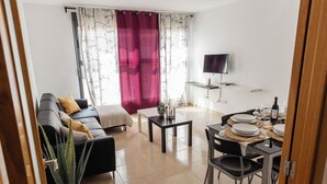 A living room with a sofa, a coffee table, and a dining area with chairs and a table set for a meal. - Apartamentos LA PARRETA CENTRO (Vinaros)