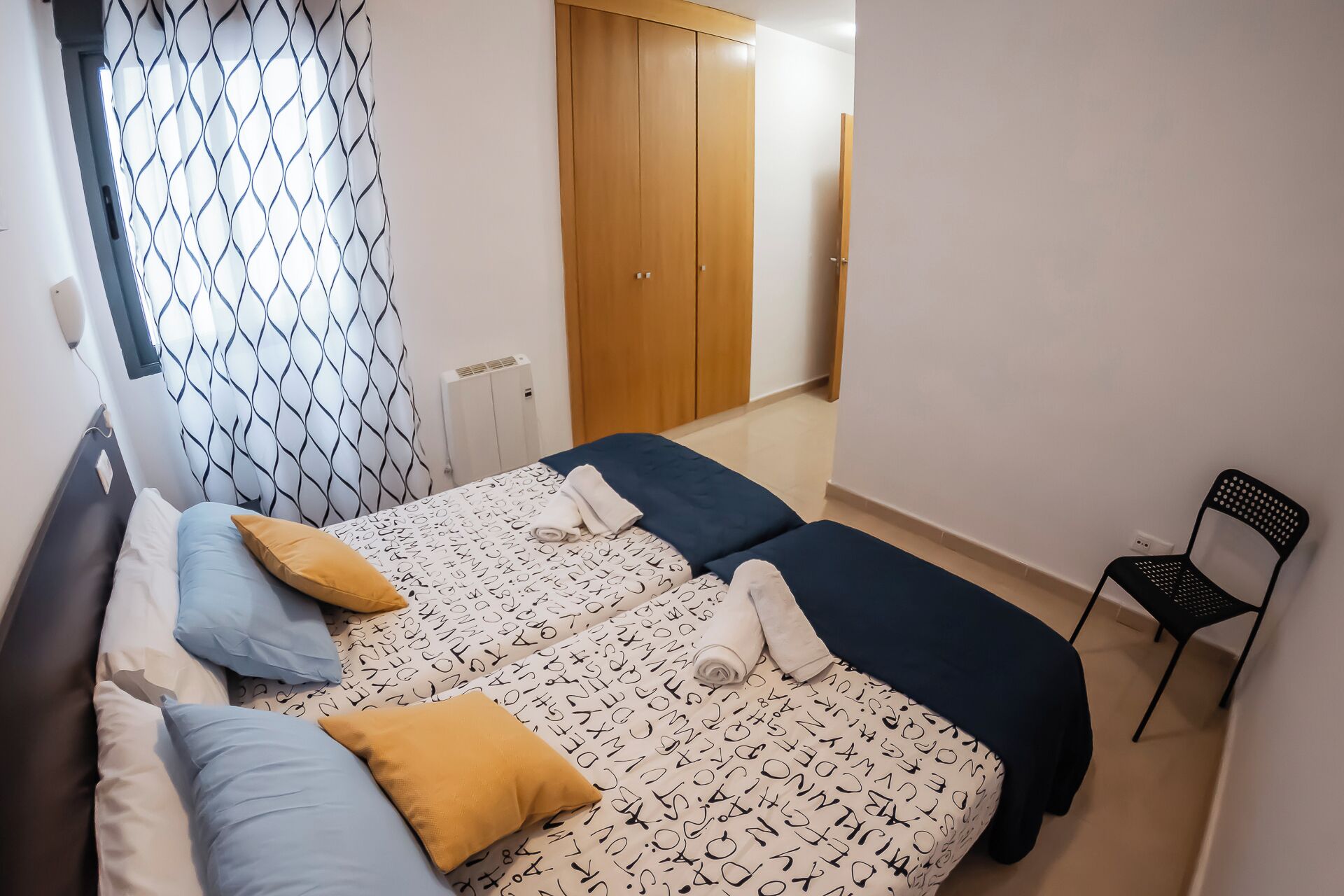A bedroom with two beds, a chair, and a wardrobe.