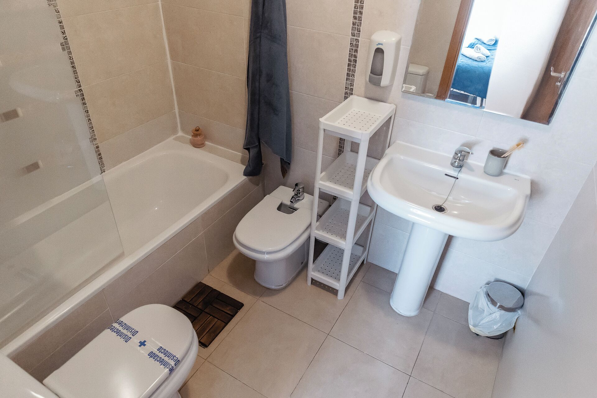 Un baño con bañera, inodoro, lavabo y una estantería.