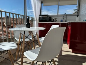 Parvekkeella on pyöreä pöytä ja tuolit, keittiö on punainen, ja parvekkeelta on näkymä katolle.