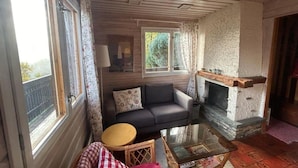A cozy living room with a fireplace, a sofa, a coffee table, and a window with curtains. - Chalet With Garden and Mountain View (Vex)