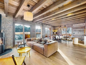 A spacious living area with a wooden ceiling, a fireplace, a sofa, and a dining area with a table and chairs.