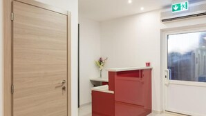 A reception area with a wooden door, a red counter, a vase with flowers, and an emergency exit sign. - Hostel Free Bird (Dubrovnik)